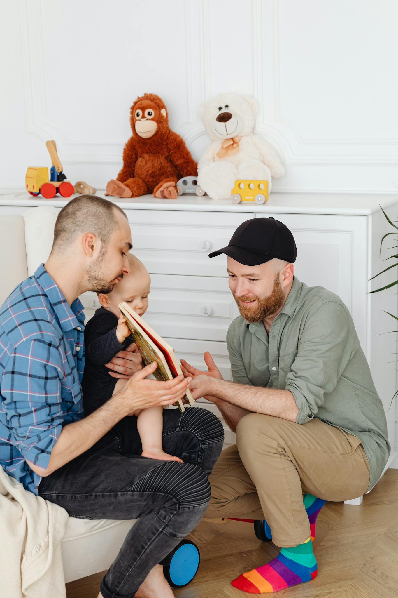 A joyful moment with two fathers bonding with their toddler indoors.